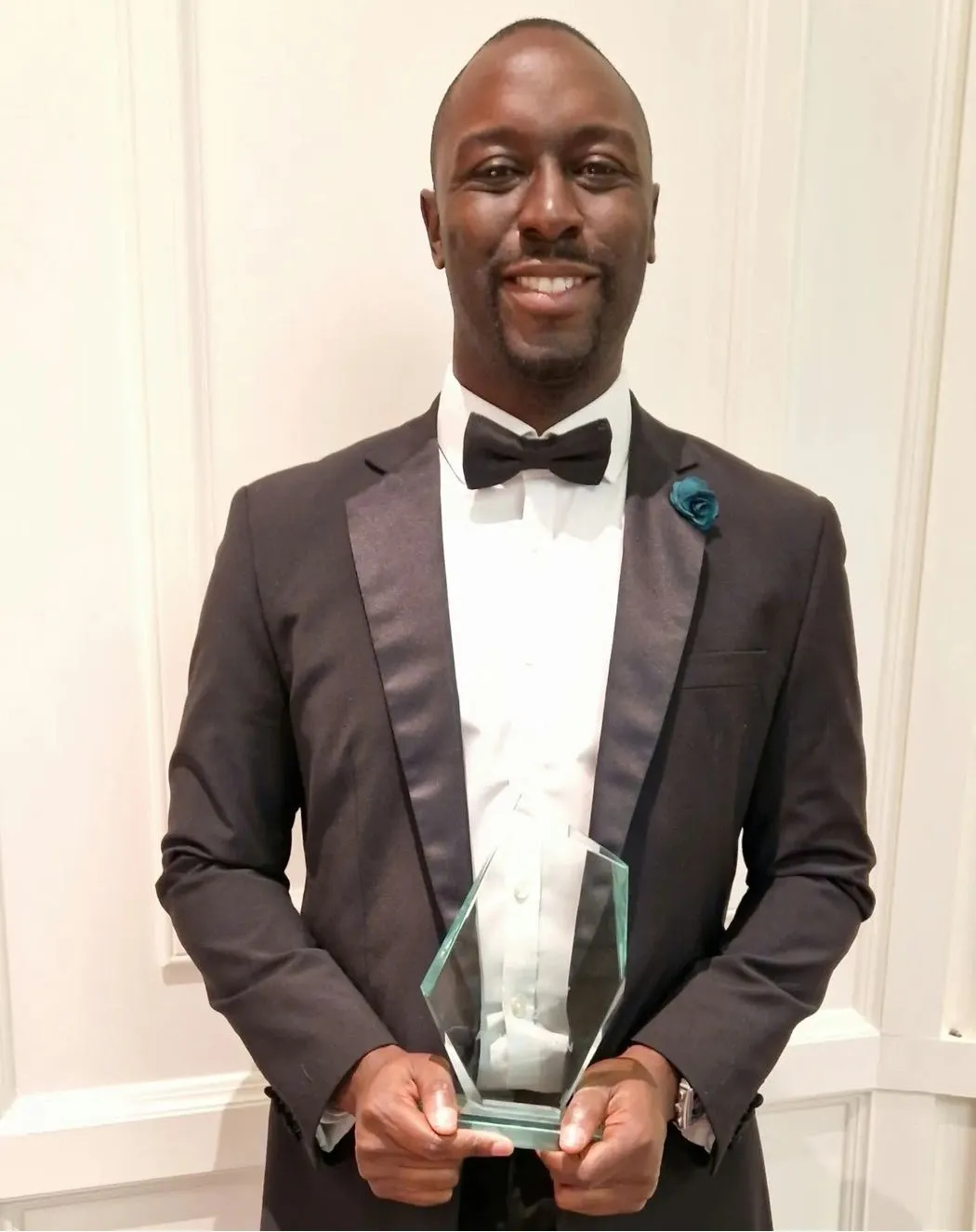 Adrian Benjamin in black tie, holding his glass award